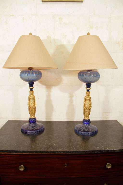 This rare pair of French Napoleon III period lamps in the Egyptian taste each has an etched blue glass base supporting a gilded metal Egyptian herm figure below an etched blue glass globular resevoir. Formerly oil lamps, they have now been fitted